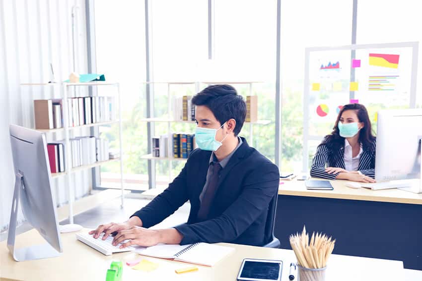 Two office workers working while wearing masks