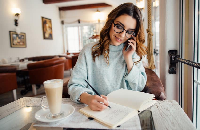 woman working from home taking notes while on a conference call