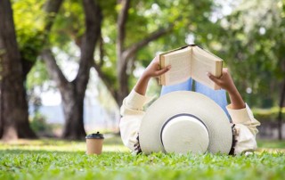 ragazza che legge un libro sdraiata sul prato nel parco durante una bella giornata di sole
