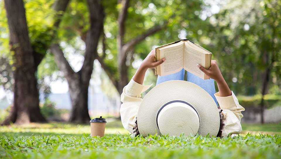 ragazza che legge un libro sdraiata sul prato nel parco durante una bella giornata di sole