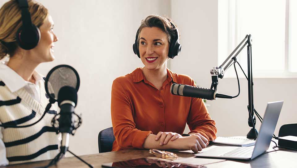 coppia di ragazze in studio che stanno registrando un podcast con microfoni e cuffie