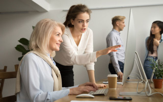 ragazza giovane junior che spiega come funziona un tool al computer a una collega senior