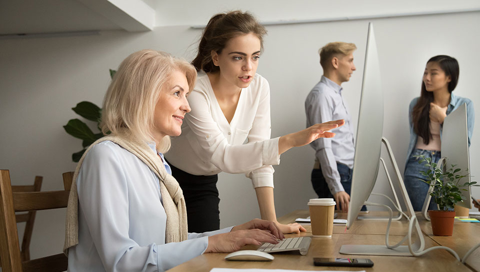 ragazza giovane junior che spiega come funziona un tool al computer a una collega senior